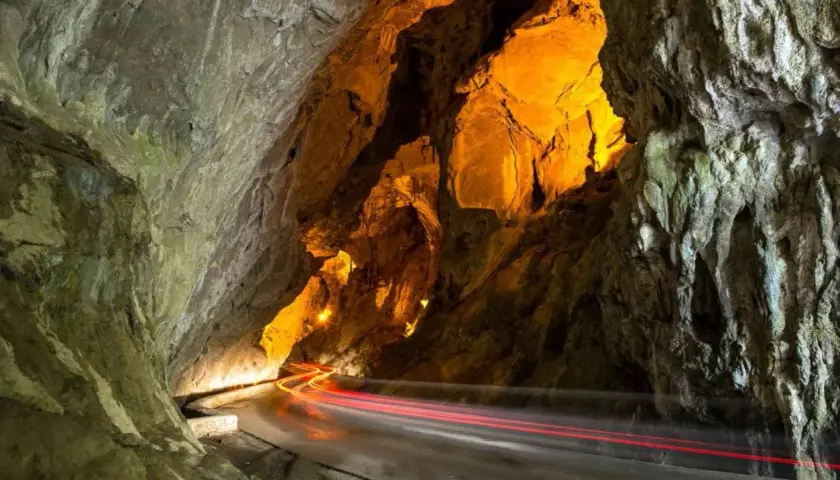 La cuevona, un túnel natural iluminado con luces cálidas, por donde pasan estelas rojas de vehículos.