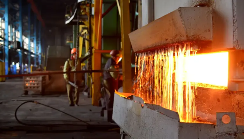 Gorący metal spływa podczas wyżarzania stali. Pracownicy w hełmach nadzorują proces w hucie.