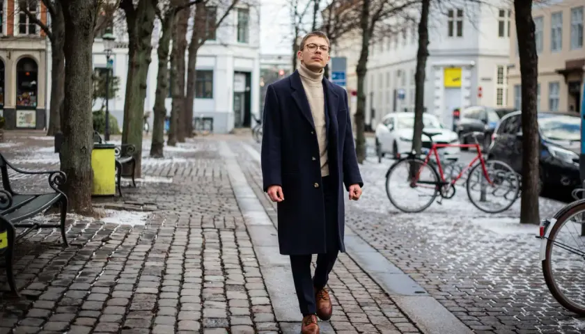 Elegancki mężczyzna w granatowym płaszczu i golfie spaceruje po zimowej ulicy. Stylowe granatowy płaszcz stylizacje na chłodne dni.