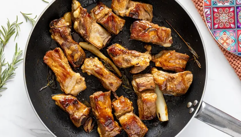 Costine di maiale in padella, dorate e succulente, con rosmarino e aglio. Un piatto invitante pronto per essere gustato.