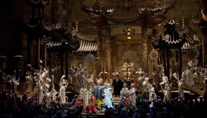 Scen från operan Turandot med en storslagen kinesisk palatsmiljö och många skådespelare i färggranna dräkter.