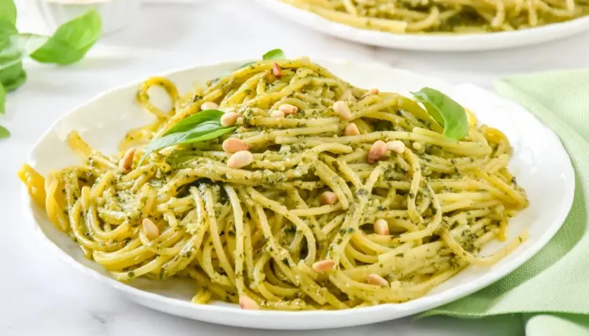Un plato de espaguetis al pesto, cubierto con piñones y hojas de albahaca fresca.