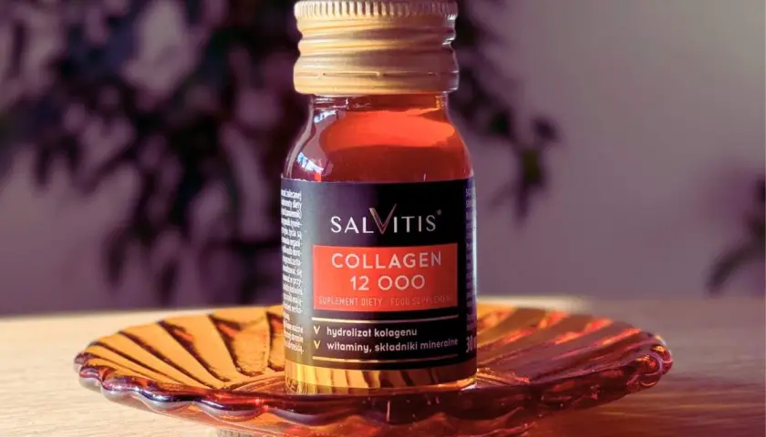 Szklana buteleczka suplementu diety SALVITIS Collagen 12 000, z płynem o bursztynowym kolorze, stoi na ozdobnej, pomarańczowej podstawce.