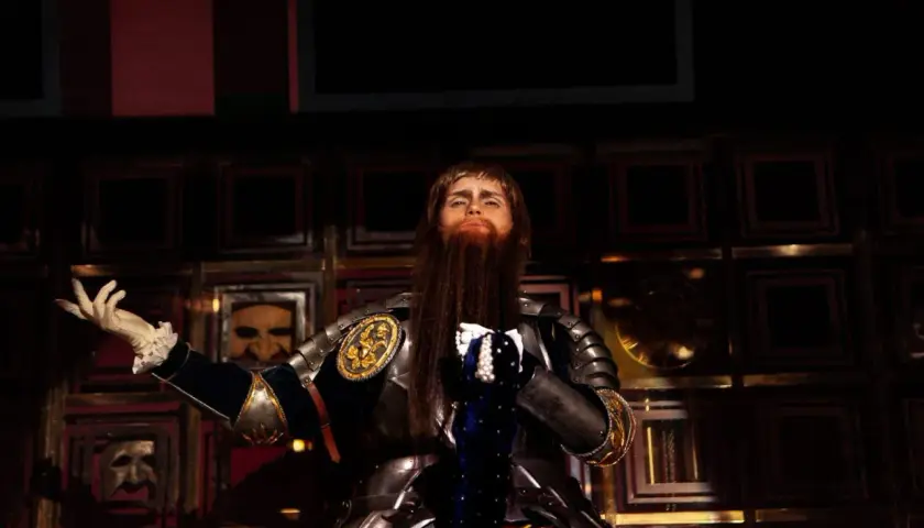 En skådespelare i rustning med långt rött skägg, som Gustav Vasa i musikalen, gestikulerar på scenen.