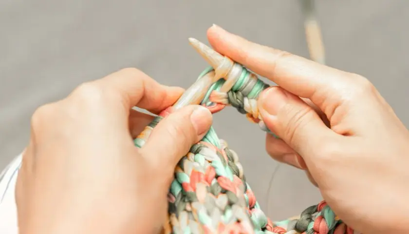 Dłonie dziergają kolorową włóczkę na drutach. Czy na Vinted można sprzedawać handmade? Tak, to świetne miejsce na rękodzieło!