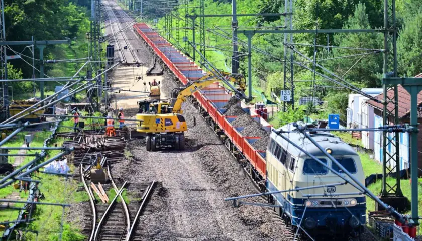 Gleisbauarbeiten: Bagger beladen einen Güterzug mit Schotter.