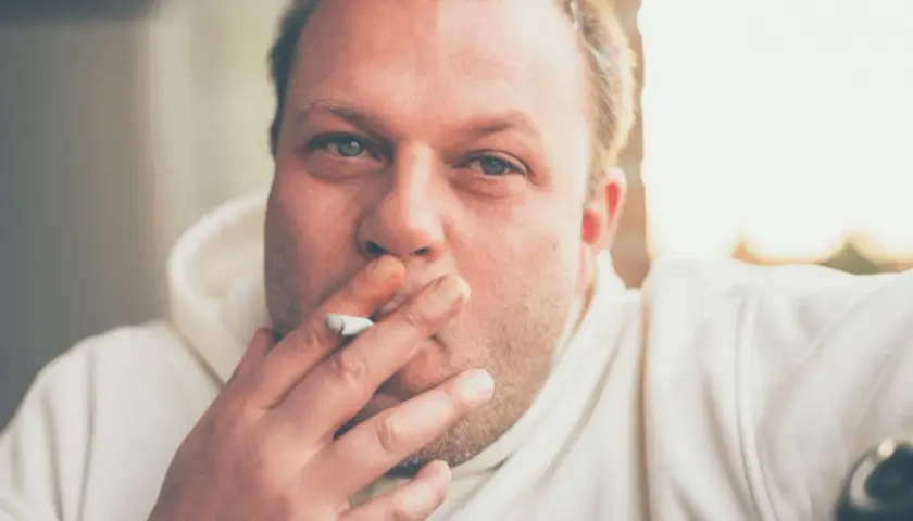 Hombre con cigarrillo en la mano, con el pelo rubio y ojos azules. Fumar hace que se te caiga el pelo.