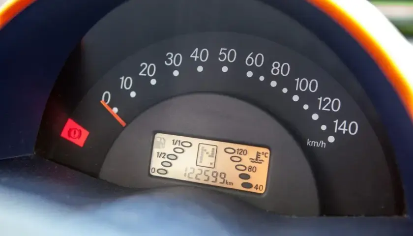 Cruscotto auto con tachimetro, indicatore carburante e spia freno a mano accesa. Chilometraggio 122599 km.