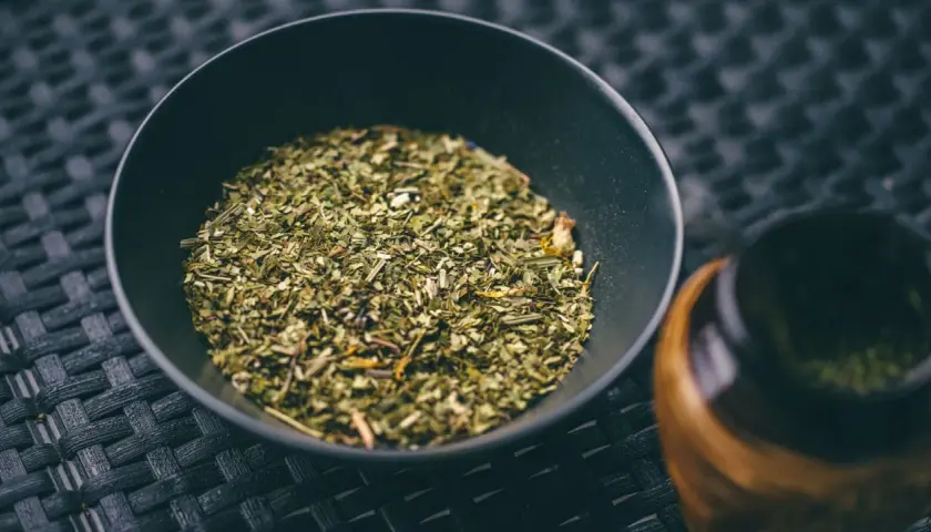 Suszone liście i gałązki, z których jest yerba mate, w czarnej miseczce obok tykwy.