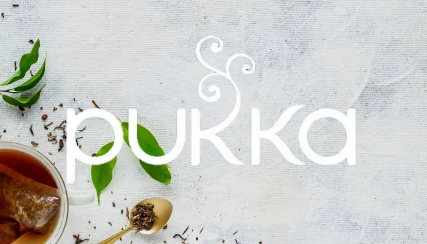 En kopp te med en tepåse, teblad och sockerbitar. Texten "PUKKA" i vitt. En sann pukka love för teälskare.