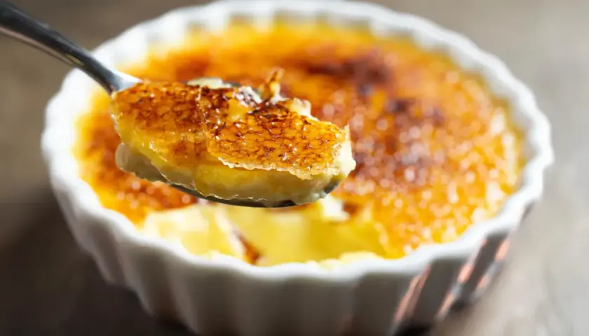 Une cuillère soulève une bouchée de crème brûlée clementine, révélant sa croûte caramélisée craquante et sa crème onctueuse.