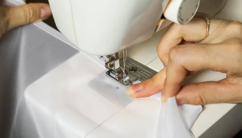 Dłonie szyją białą tkaninę na maszynie do szycia.