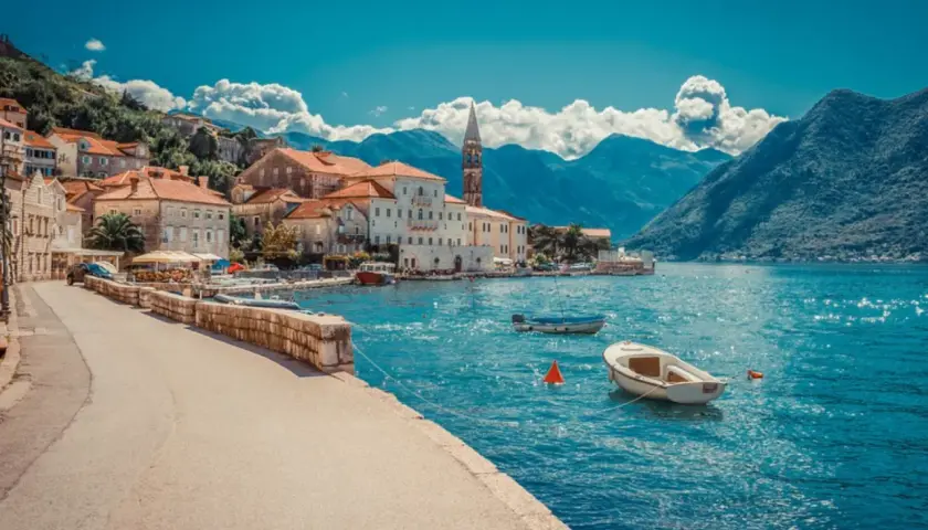 Blick auf eine malerische Küstenstadt mit roten Dächern und einem Kirchturm, umgeben von Bergen. Boote schaukeln auf dem türkisfarbenen Wasser. Ein Traumziel!