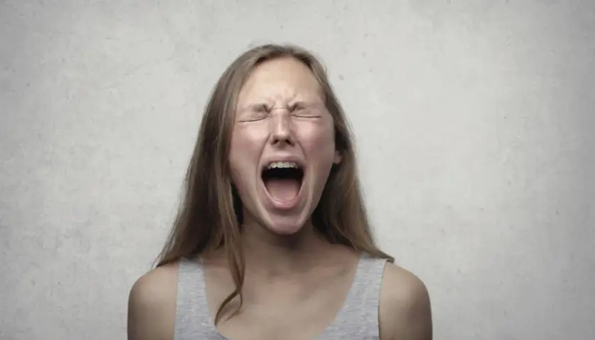 Ragazza con apparecchio dentale urla, occhi chiusi e fronte corrugata, un'espressione di pura paura di perdere il controllo.