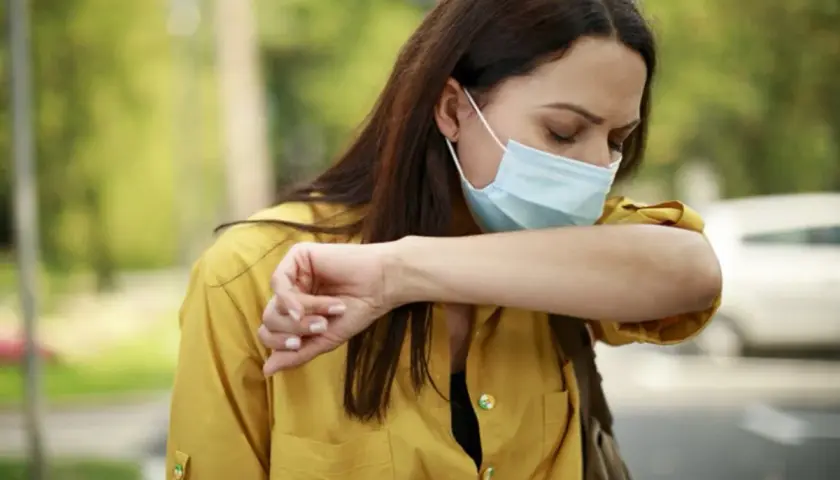 Mujer con mascarilla quirúrgica para que sirve, tose en el codo para evitar contagios.