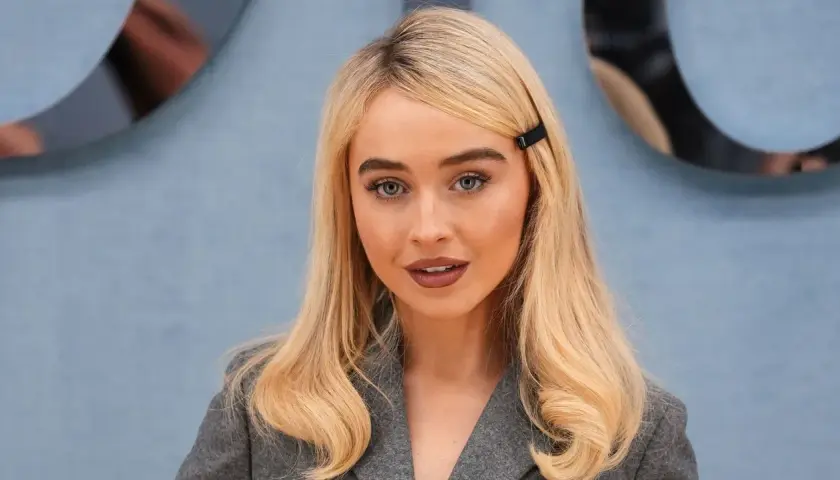 Mujer rubia con raya del pelo lateral, ojos azules y un clip negro en el cabello.