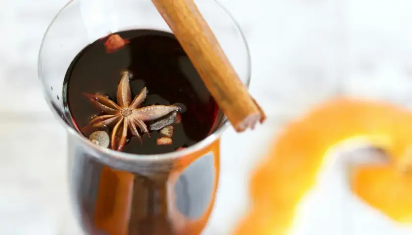 Un verre de vin chaud aux épices, parfait pour un marché de Noël. Une étoile de badiane et un bâton de cannelle flottent dans le liquide sombre.