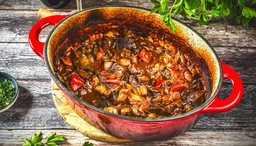 Herzhaftes Kalbsgulasch im roten Bräter, ein köstliches Rezept mit Paprika und Zwiebeln, bereit zum Servieren.