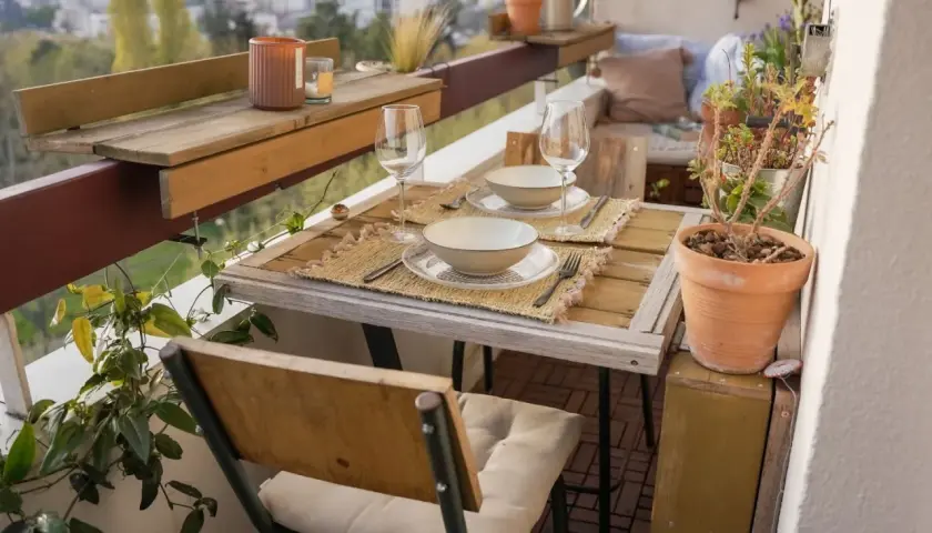 Jolie deco balcon avec table dressée pour deux, plantes vertes et vue sur la ville. Parfait pour un dîner romantique.