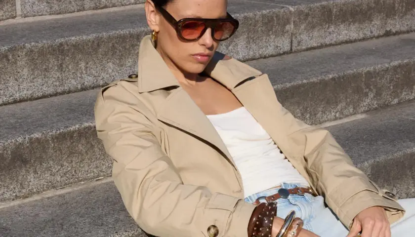 Mujer con gabardina beige y gafas de sol, lista para la moda primavera.