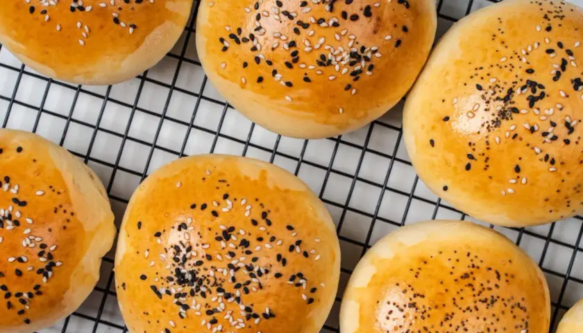 Złociste bułeczki do mini burgerów posypane sezamem i czarnuszką, na czarnej kratce.