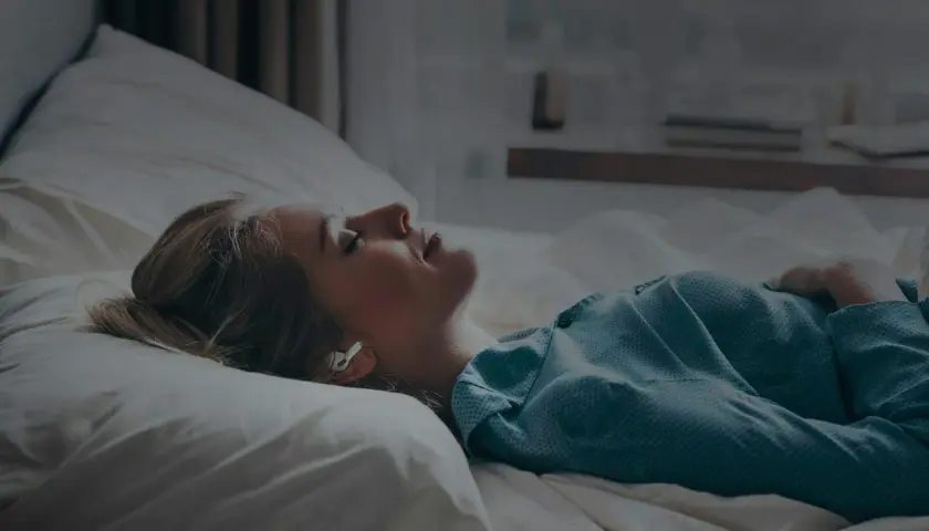 Kvinna med hörlurar i sängen, lyssnar på guidad meditation för avkoppling.