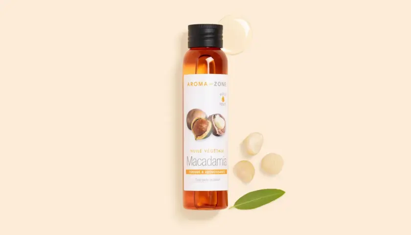 Flacon d'huile de macadamia, ses bienfaits pour la peau sont nombreux. Noix et feuille à proximité.