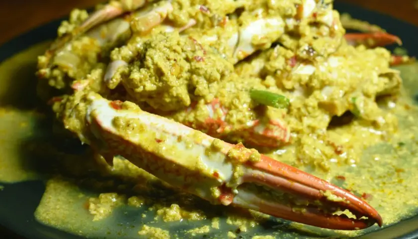 Krab w żółtym sosie curry na czarnym talerzu.