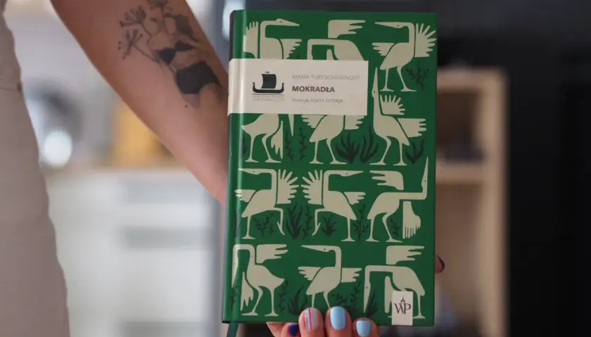 Zielona okładka książki "Mokradła" Marii Turtshaninoff, z ptakami i roślinami, symbolizuje mrok i naturę, przyczyny sukcesu literatury skandynawskiej w Polsce.