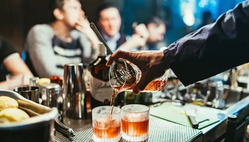 Un barman prépare un cocktail de base, versant un liquide ambré dans deux verres.