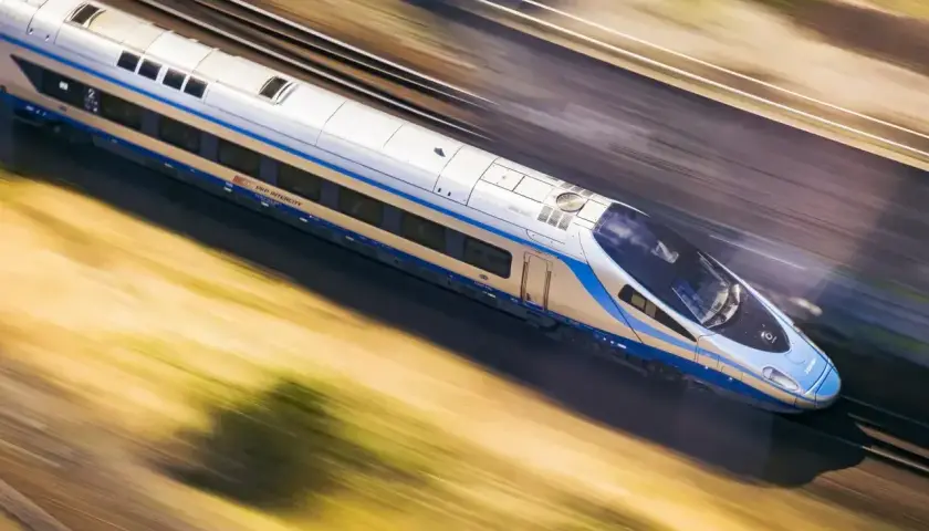 Srebrno-niebieski pociąg PKP Intercity mknie po torach, ukazując imponującą prędkość pociągu.