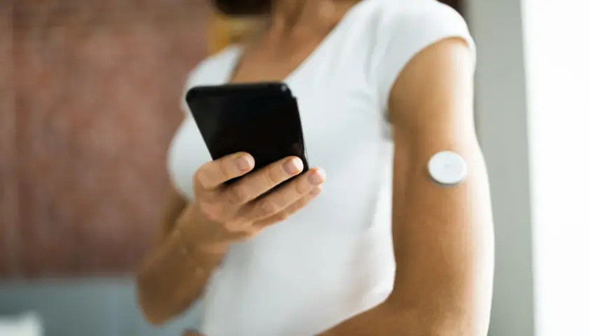 Kobieta z sensorem na ramieniu korzysta z aplikacji Libre 2 na telefonie, monitorując swoje zdrowie.