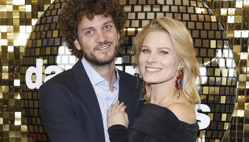 Anna Głogowska z partnerem pozują na tle błyszczącej, złotej ściany.