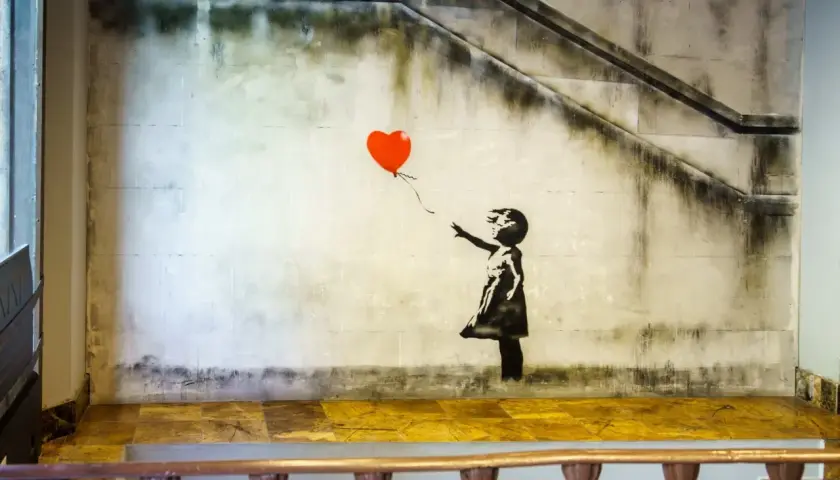 Dziewczyna z balonami, Banksy. Dziecko w czarnej sukience sięga po czerwony balon w kształcie serca na tle zniszczonej ściany ze schodami.