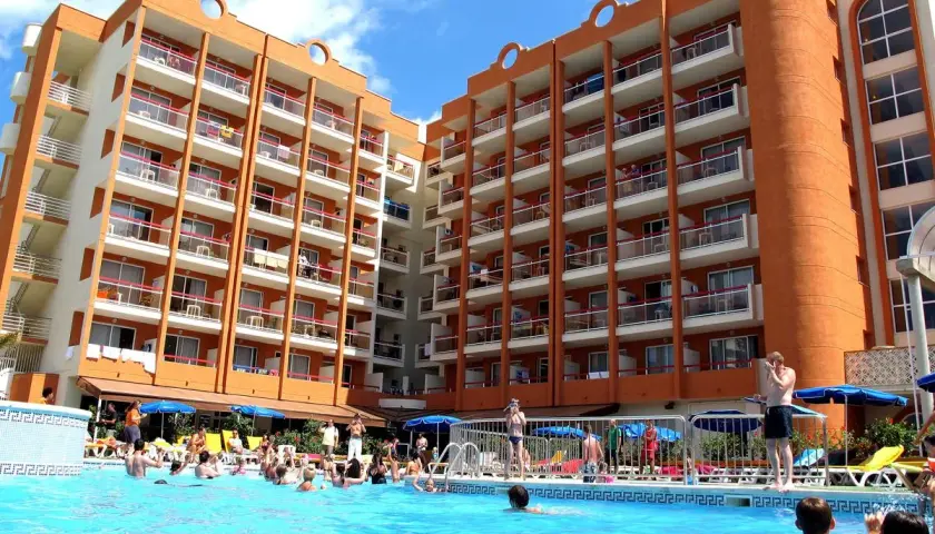 Gente disfrutando en la piscina del hotel Belvedere Salou, con edificios naranjas y blancos de fondo.