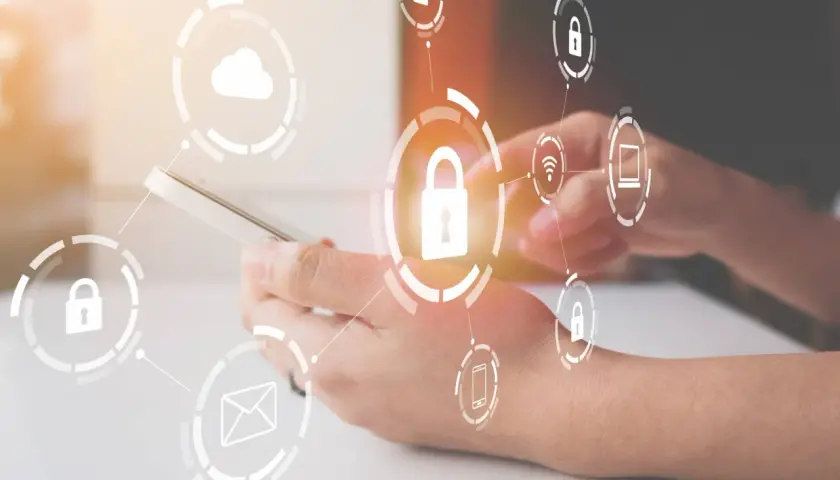 Manos sujetando un teléfono con iconos de seguridad y dispositivos de almacenamiento conectados, simbolizando la protección de datos.