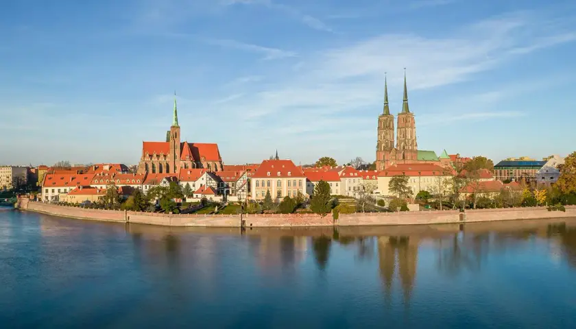 Widok na Ostrów Tumski, serce starego miasta Wrocławia, z katedrą i kościołem św. Krzyża odbijającymi się w spokojnej wodzie Odry.
