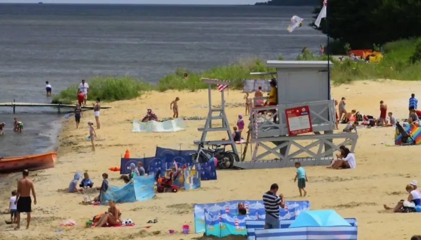 Słoneczna puck plaża tętni życiem. Ludzie opalają się, kąpią i bawią, tworząc radosną atmosferę.