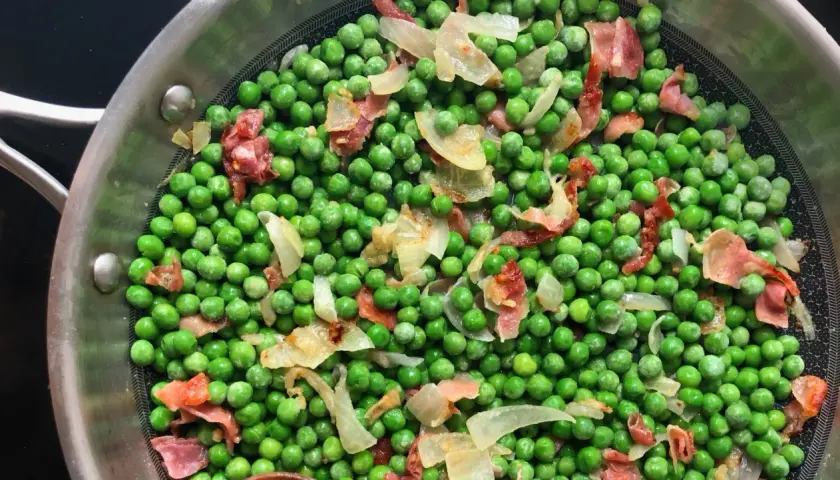 Guisantes con jamón y cebolla en una sartén. Un plato sencillo y delicioso.