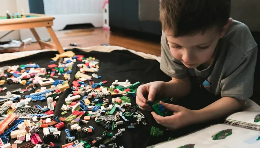 Chłopiec buduje z klocków LEGO, a obok leży instrukcja. Jak umyć klocki LEGO? Wystarczy je zebrać i umyć.