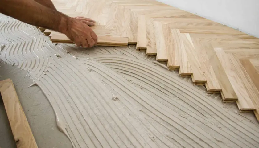 Pose de parquet en chevrons. Des lames de bois clair sont posées sur un lit de colle ondulée.