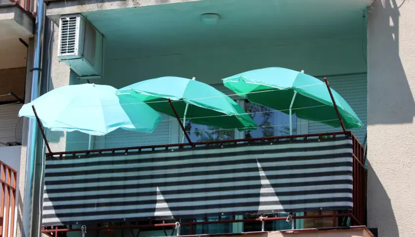 Trzy turkusowe parasole nad zasłoniętą balustradą na balkonie. Pomysł, jak zasłonić balustradę na balkonie, wykorzystując parasole.