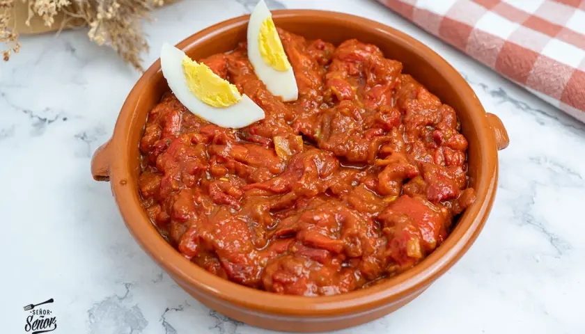 Un plato de asadillo manchego, con pimientos rojos guisados y adornado con gajos de huevo cocido.