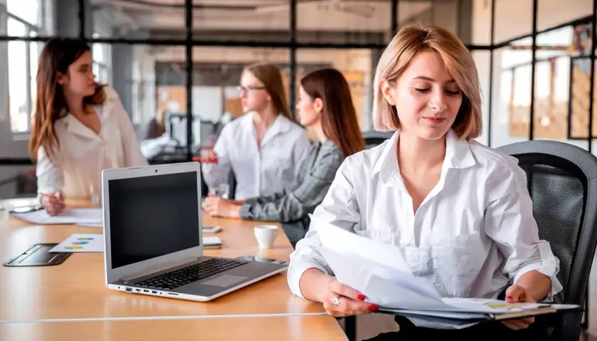 Kobiety w biurze pracują nad projektem. Jedna z nich, blondynka, przegląda dokumenty. To idealna templatka do wizualizacji pracy zespołowej.