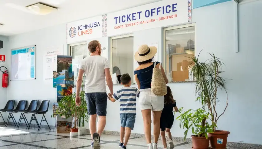 Famiglia in coda all'ufficio biglietti per la Corsica con bambini. L'avventura inizia qui!