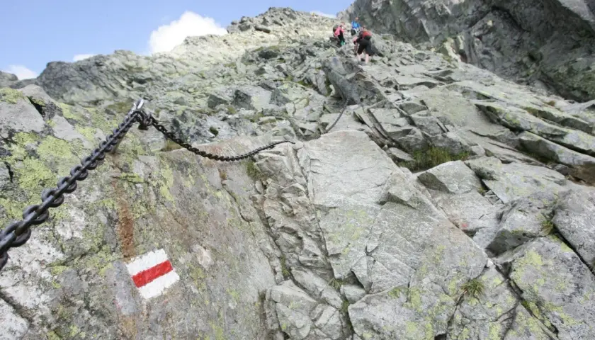 Łańcuchy i czerwono-białe oznaczenia szlaków na skalistym zboczu, wskazujące na jedne z najtrudniejszych szlaków w Tatrach.