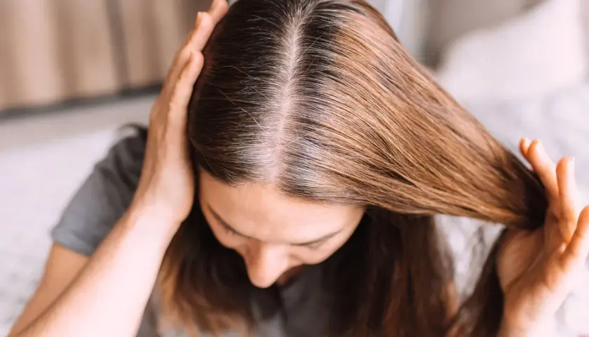 Una mujer se toca el cabello, mostrando mechones grises que explican porque salen canas.