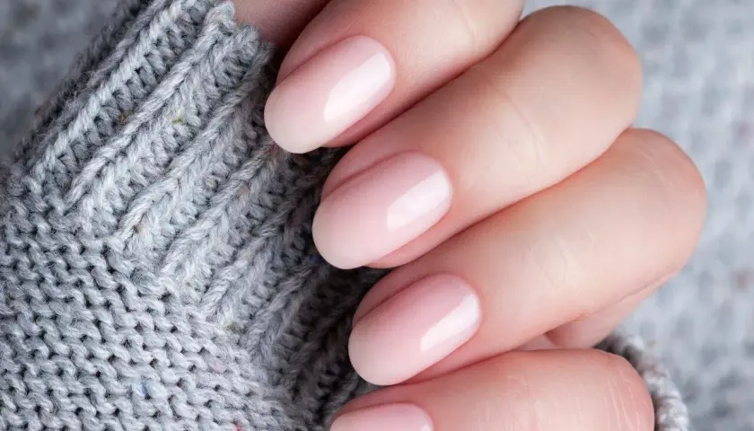 Dłoń z delikatnym, różowym manicure. Czy baza kauczukowa niszczy paznokcie? Zdjęcie sugeruje, że nie, jeśli jest stosowana prawidłowo.