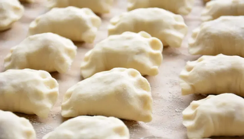 Gotowe do gotowania pierogi ruskie, przygotowane według tradycyjnego przepisu. Widać je ułożone rzędami na blacie.