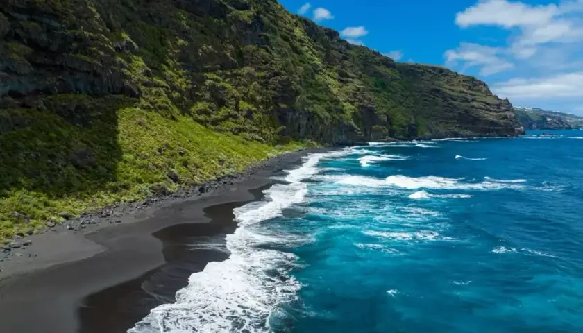 Costa salvaje con arena negra y mar azul intenso, un rincón idílico de las playas de Canarias.